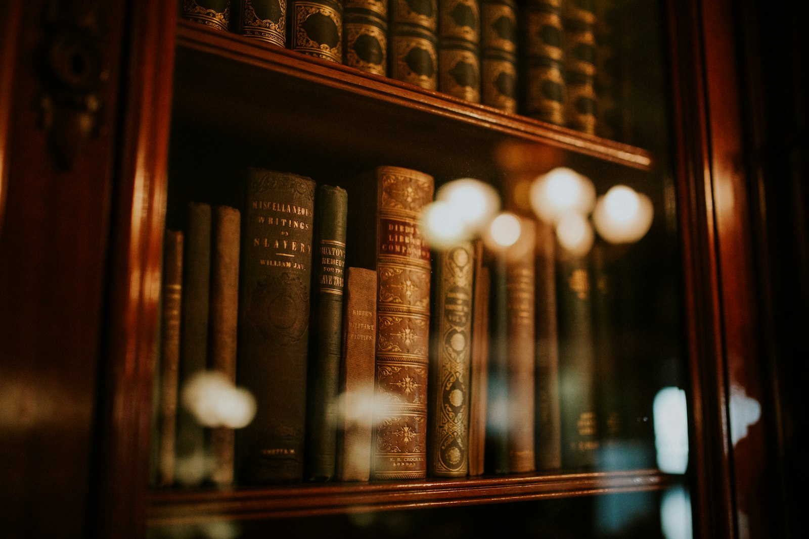 Old leather-bound books behind glass in a warmly lit bookcase